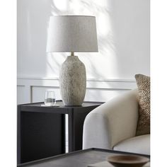 a white vase sitting on top of a table next to a lamp and a couch