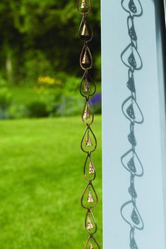 a metal wind chime hanging from the side of a building in front of grass