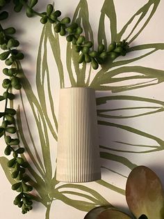 an arrangement of green leaves and flowers on a white wall with a vase in the middle