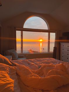 the sun is setting over the ocean through an arched window in a bedroom with white bedding