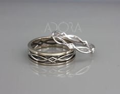 two silver rings with leaves on them sitting on top of a gray surface and the words ascoa written in white gold