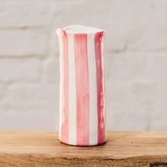 a pink and white striped vase sitting on top of a wooden table next to a brick wall