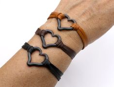 a person's arm with two leather bracelets on it and one has an interlocked heart