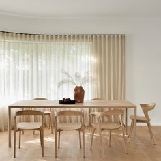 a dining room table with chairs and a vase on top of it in front of a curtained window