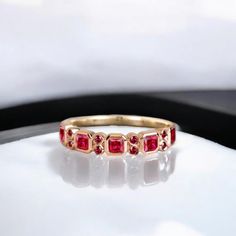 a gold ring with three red stones on the front and side, sitting on a white surface