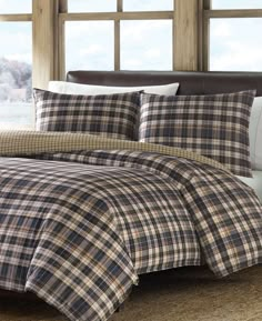 a bed in a bedroom with plaid comforter and pillows