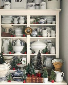 a white china cabinet filled with dishes and christmas tree decorations on top of it's shelves