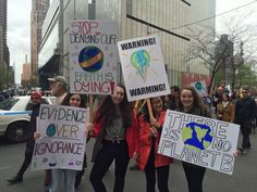 four girls holding signs in the middle of a street with other protestors behind them