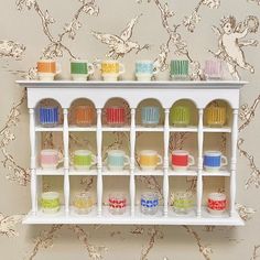 a white shelf filled with cups and saucers on top of a wallpapered wall