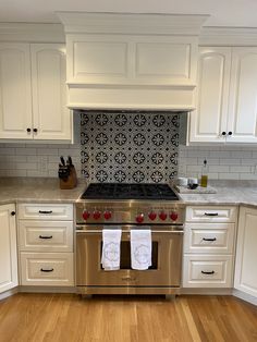 a stove top oven sitting inside of a kitchen next to white cabinets and wooden floors