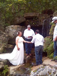 a bride and groom standing in front of a waterfall with their wedding party holding hands