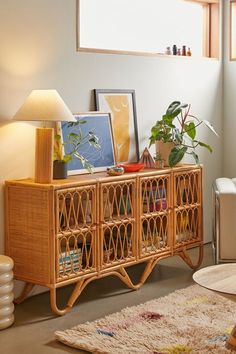 a living room with plants and pictures on the sideboard next to a rug in front of a window