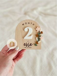 a person holding up a wooden sign with flowers on it that says 2 eief