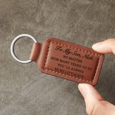 a hand holding a leather keychain that says to my son, no matter how many years go by you'll always be my little son