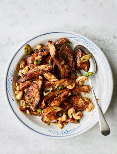 a white plate topped with chicken and cashews on top of a marble counter