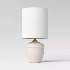 a white table lamp with a white shade on the base and a light bulb attached to it