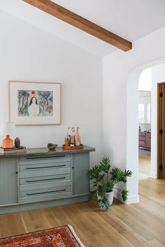 a living room with wood floors and a painting hanging on the wall over a gray cabinet