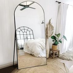 a mirror sitting on top of a rug next to a bed in a white room