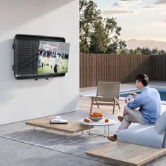 a man sitting on a couch watching tv in the backyard with his feet propped up