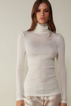 Long-sleeve high-neck tubular top made from a wool-silk blend. Elegant Stretch White Turtleneck, Elegant White Stretch Turtleneck, Elegant White High Neck Turtleneck, Fitted Fine Knit Merino Wool Tops, Fitted Merino Wool Fine Knit Tops, Classic Turtleneck Top In Winter White, Elegant Winter White Fine Knit Top, Classic Winter White Turtleneck Top, Elegant High Neck Tops For Winter