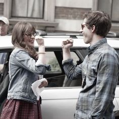 a man and woman standing next to each other in front of a car with their fists raised