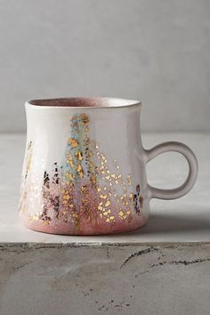 a white and pink coffee cup with gold sprinkles on the inside sits on a countertop