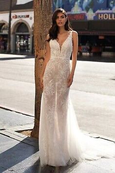 a woman standing next to a tree wearing a wedding dress