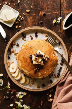 a stack of pancakes on a plate with banana slices and chocolate chips next to it