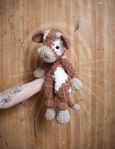 a hand holding a stuffed animal on top of a wooden floor next to a person's arm