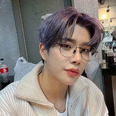 a young man with purple hair and glasses looking at the camera while wearing a sweater