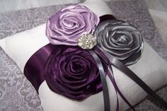 the pillow is decorated with purple and silver fabric flowers on top of it, along with a satin ribbon