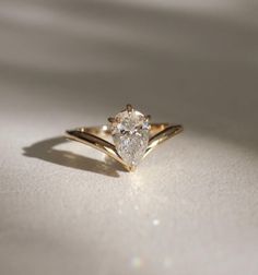 a yellow gold ring with a pear shaped diamond in the center on a white surface