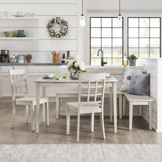 a kitchen with white walls and wooden flooring next to a dining table surrounded by chairs