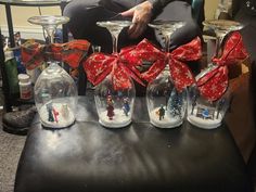 four wine glasses with red bows are sitting on a black leather ottoman in front of a christmas scene