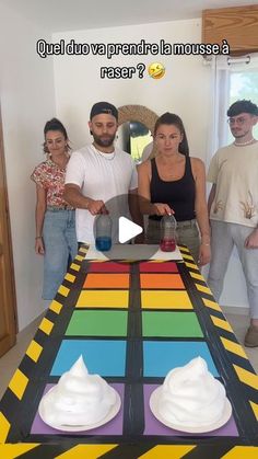 a group of people standing in front of a rainbow colored table with whipped cream on it