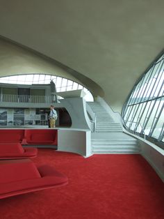 a red carpeted room with stairs leading up to the second floor and a man standing in the doorway