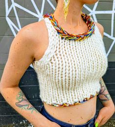 a woman with tattoos wearing a white knitted crop top and blue denim shorts standing in front of a graffiti wall