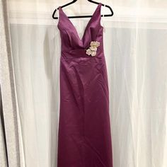 a purple dress hanging on a hanger in front of a white wall and curtain