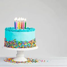 a blue birthday cake with sprinkles and lit candles on the top is surrounded by confetti