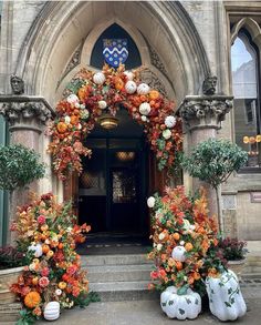 an entrance decorated with pumpkins, flowers and greenery in front of a church