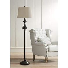 a white chair sitting next to a lamp on top of a hard wood floor in front of a white wall