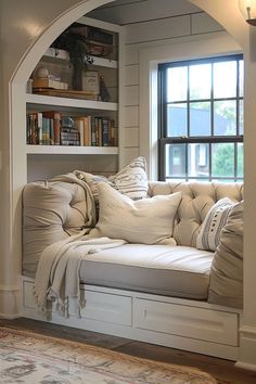 a white couch sitting under a window next to a book shelf with books on it