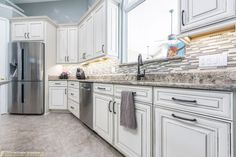 a kitchen with white cabinets and granite counter tops, stainless steel refrigerator and dishwasher