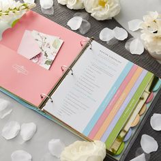 an open planner book sitting on top of a table next to white flowers and petals