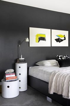 a bedroom with two paintings on the wall and a bed in the foreground, next to a white trash can