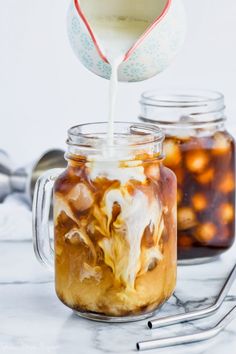 a glass jar filled with liquid and ice cream on top of a table next to a spoon