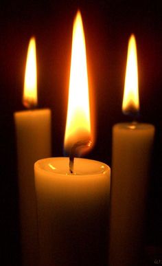 three lit candles in front of a dark background