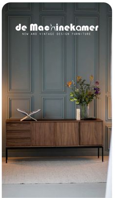 a vase with flowers sitting on top of a wooden cabinet in front of a wall