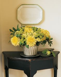 a black table with a metal bucket filled with yellow flowers sitting on top of it