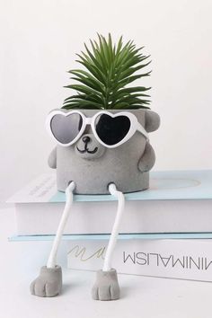 a stuffed animal with sunglasses on top of a stack of books and a potted plant